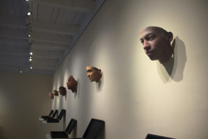 An assortment of masks hung up on the wall inside an art gallery. The masks are part of an exhibition called "Stranger Visions" by Heather Dewey-Hagborg.